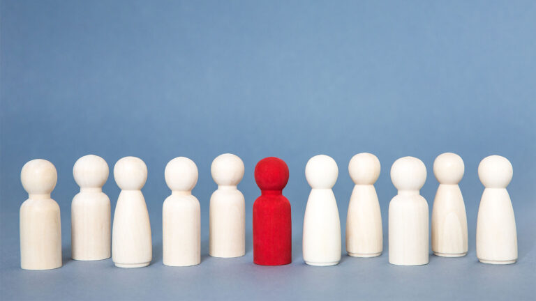 11 wooden pegs roughly human form, 1 red, 10 white