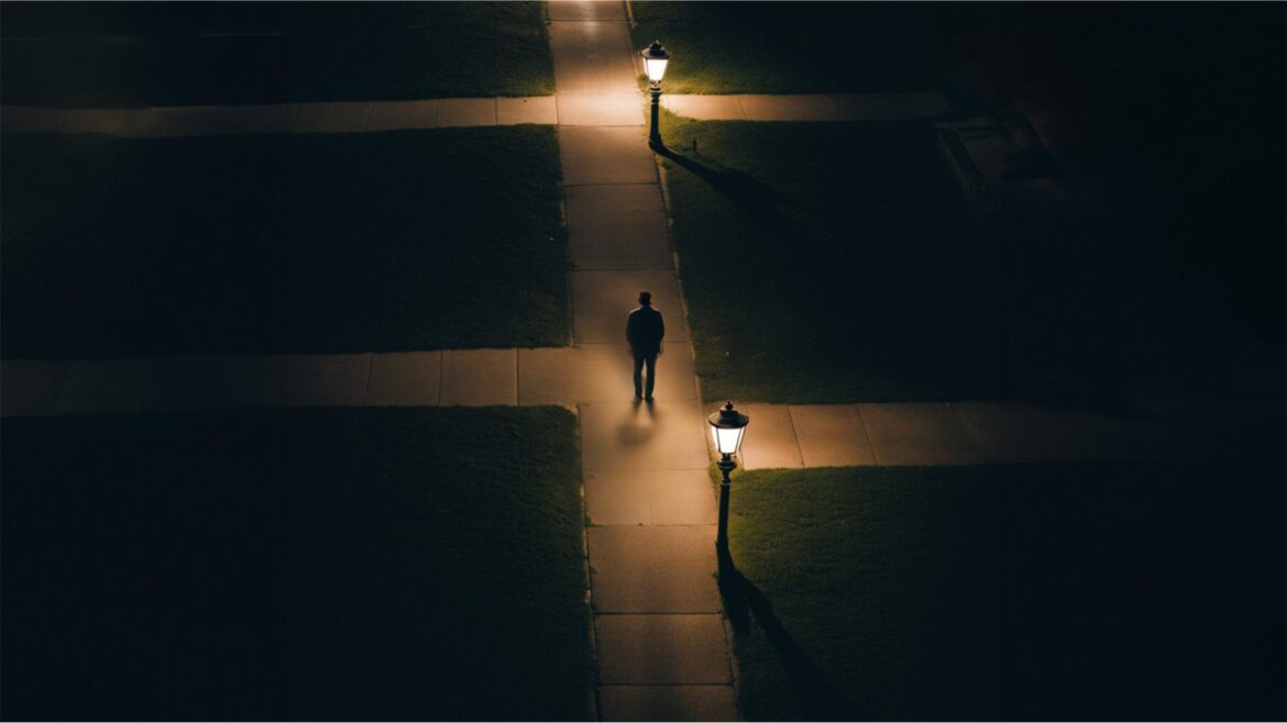 Nighttime image from above showing a person walking along a sidewalk with paths leading off to each side, lit by lamps long the path.