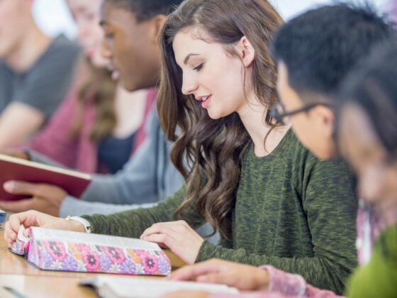 Looking down a line of students in class as they read open Bibles on their desks.