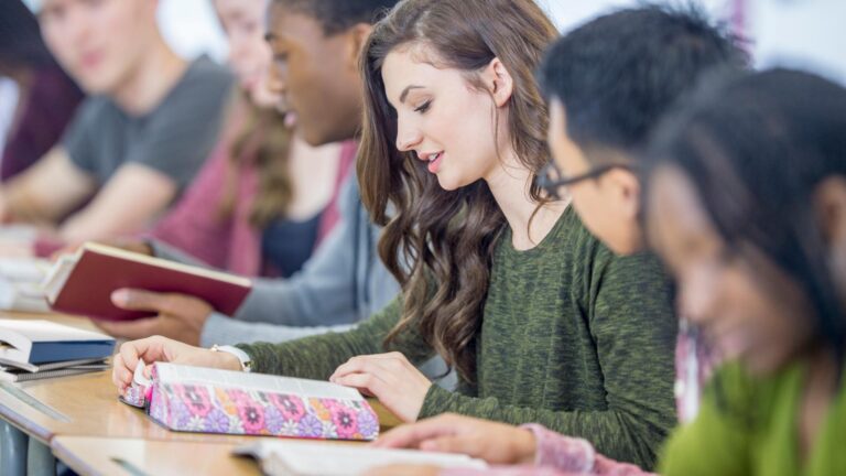 Looking down a line of students in class as they read open Bibles on their desks.