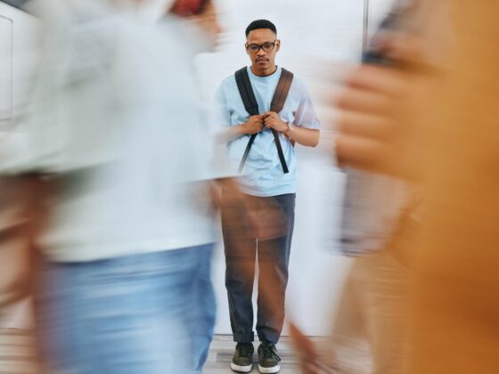 Young man with school backback in background viewed through blurred images of other students.