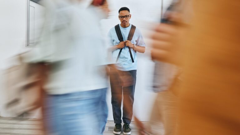 Young man with school backback in background viewed through blurred images of other students.