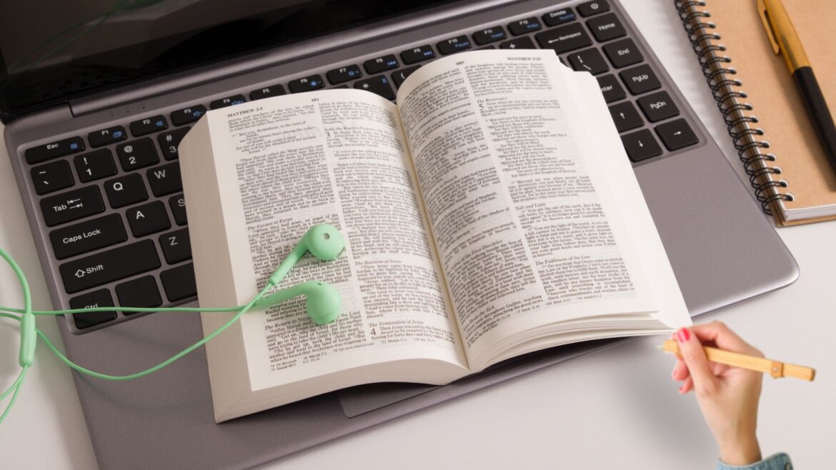 Open bible on a keyboard, with green ear buds on top.