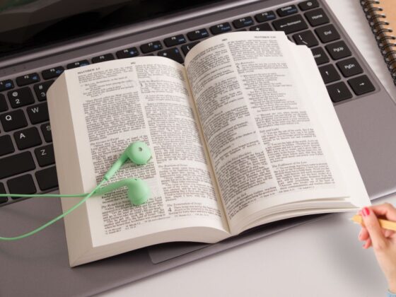 Open bible on a keyboard, with green ear buds on top.