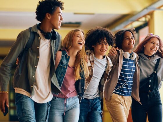 5 young adults with arms around each other walking down a hallway and smiling broadly