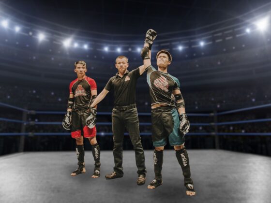 3 young men in a fighting ring dressed as competitors and referee with the referee raising the hand of one man as victor