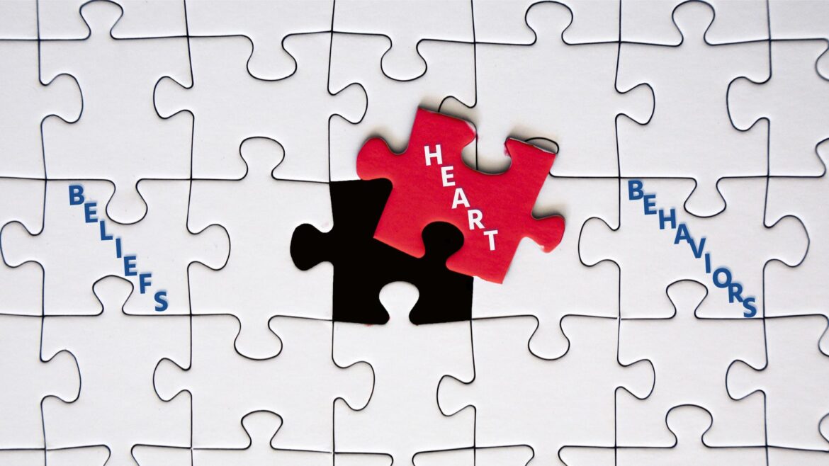 White puzzle pieces, with the center one in red, labeled "heart" and to other white pieces labeled "beliefs" and "behaviors."