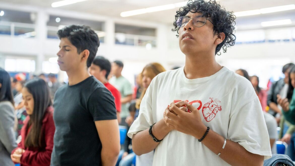 A brightly lit room full of young people in worship.