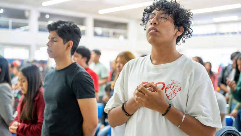 A brightly lit room full of young people in worship.