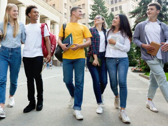 6 young adults walking into frame on a school campus