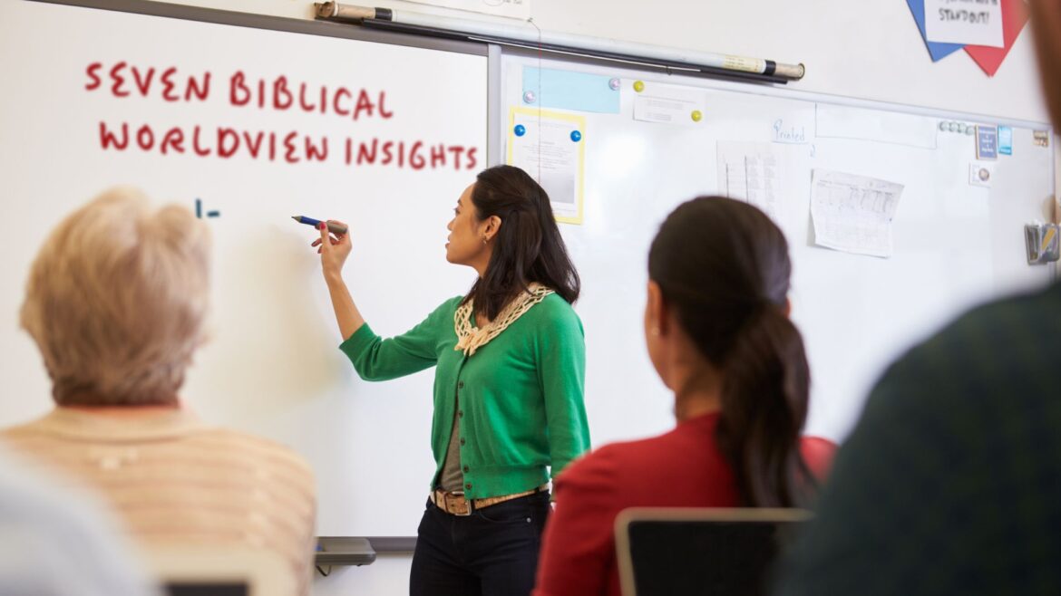 Female teacher stands writing on whiteboard at front of classroom, "7 biblical worldview insights"