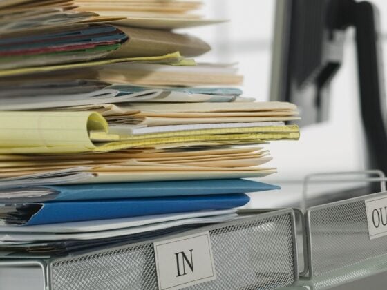 A stack of papers and folders piled high in an office inbox beside an empty outbox.